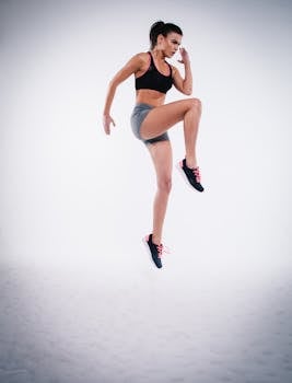 Woman in black sports bra and gray shorts performing a jump during workout.