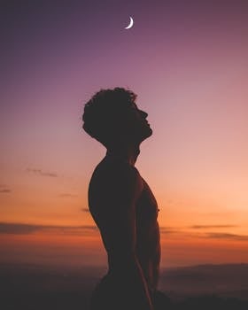 Silhouette of a man looking up at a crescent moon against a colorful twilight sky, creating a dramatic scene.
