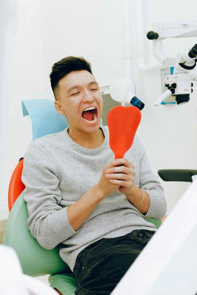 A man sits smiling in a dental clinic chair holding a mirror during a dental check-up.