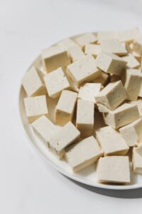 High-angle view of fresh cubed tofu arranged on a white plate, showcasing texture and simplicity.